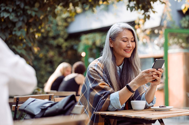 Mujer sonriendo mientras mira su teléfono en una cafetería