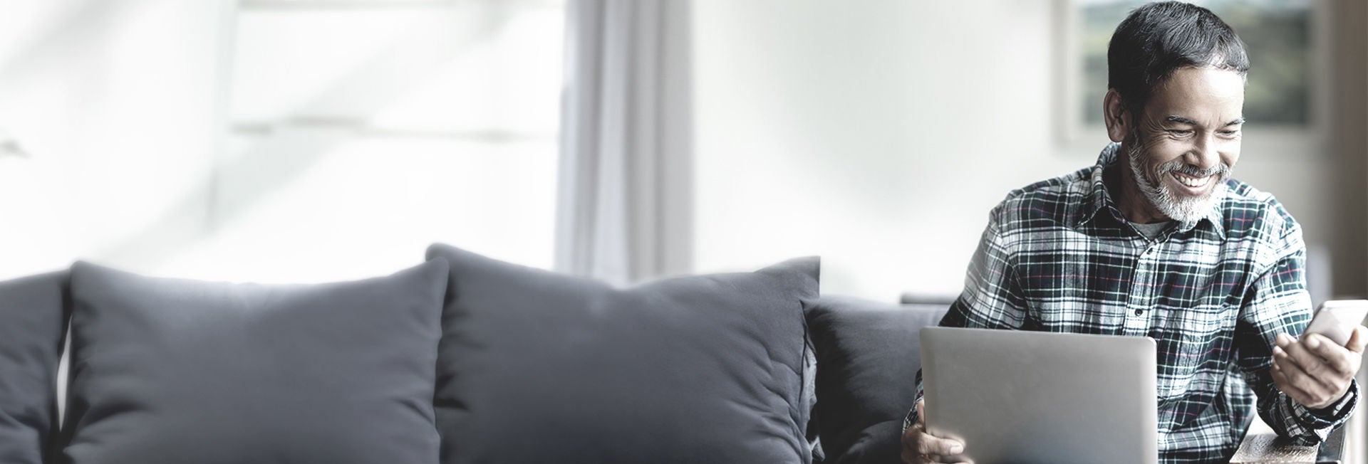 Un hombre sonriendo mientras usa el ordenador portátil y el teléfono en casa