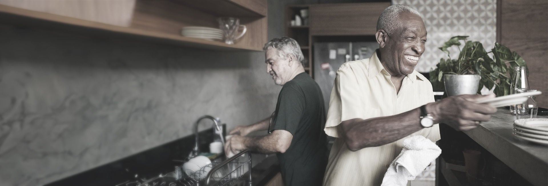 Dos hombres mayores sonriendo mientras lavan los platos en una cocina